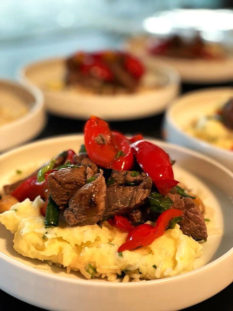 Eine Schale mit cremigem Kartoffelpüree, garniert mit saftigem Rindfleisch und frischen roten Paprika.