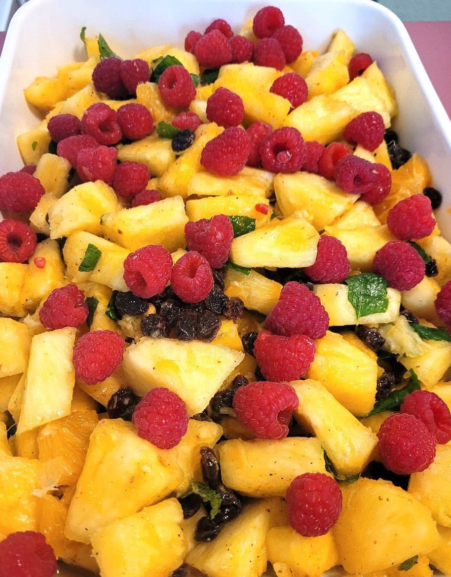 Frischer Obstsalat mit Ananas, Himbeeren und Minze in leuchtenden Farben in einer weißen Schale.