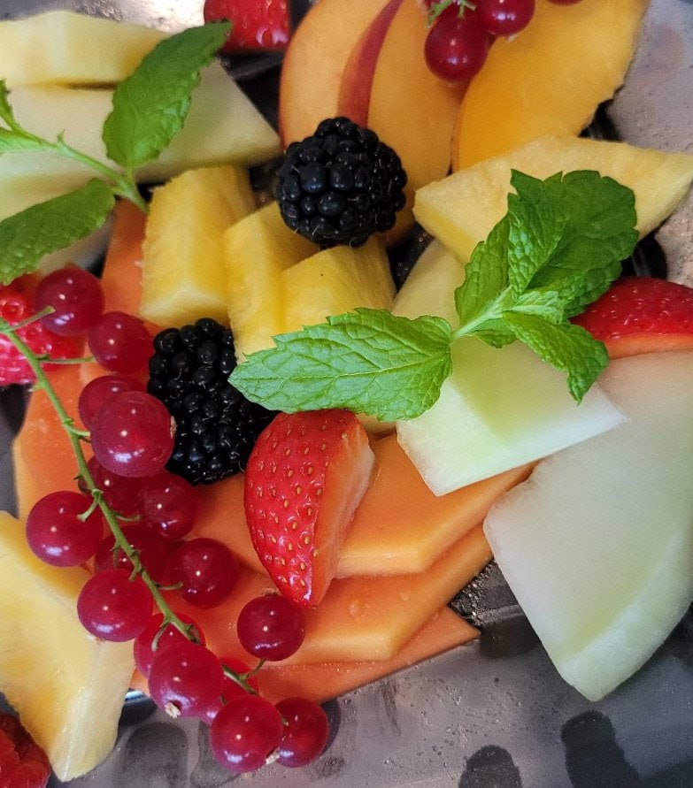 Bunter Obstsalat mit Beeren, Melonen und Minzblättern in leuchtenden Farben.