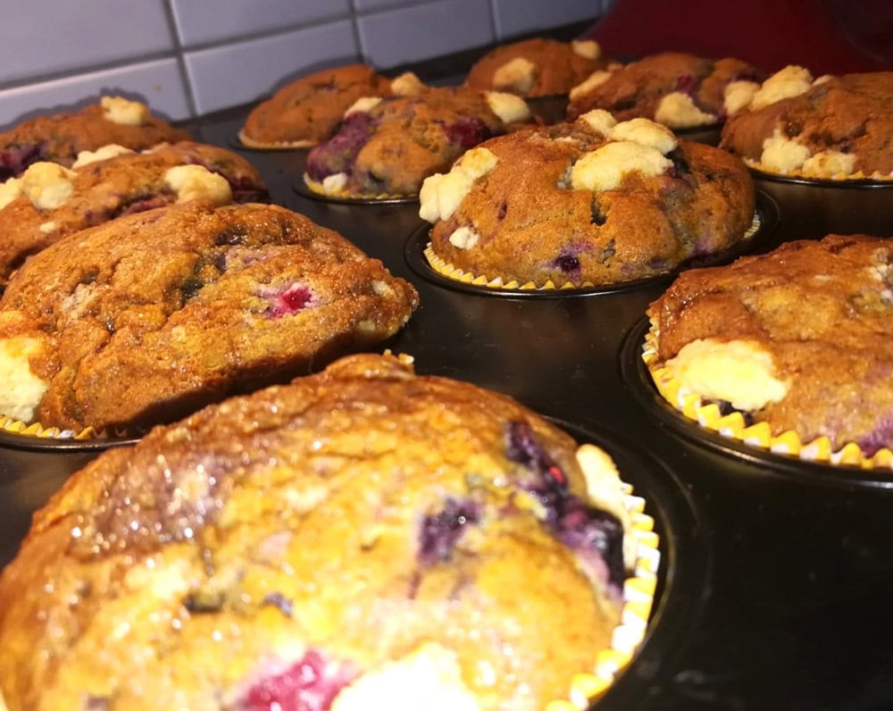 Frisch gebackene Beerenmuffins mit knusprigen Streuseln auf einem Backblech.