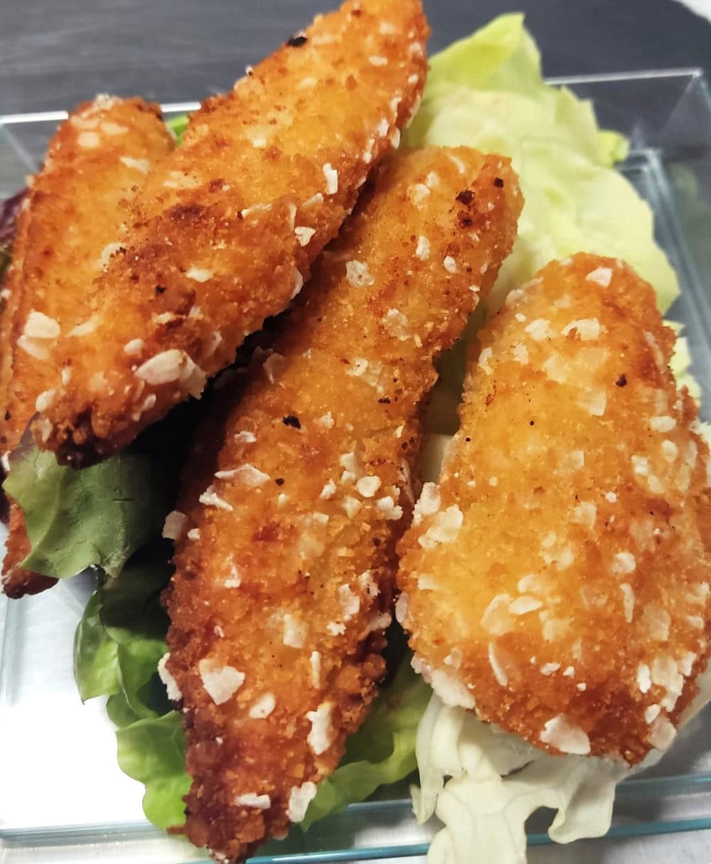 Knusprige, goldbraune Hähnchennuggets auf grünen Salatblättern auf einem Teller.