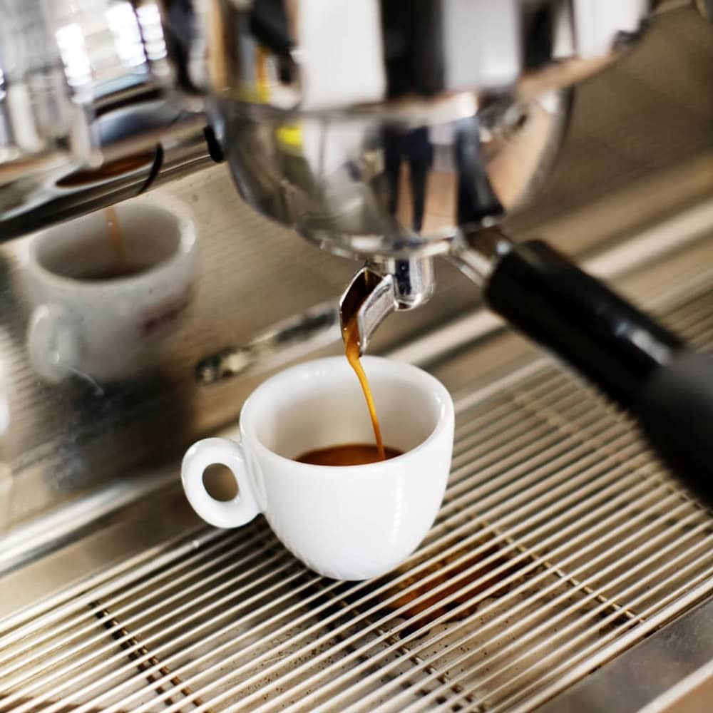 Espresso läuft in weiße Tasse unter Chrom-Espressomaschine.