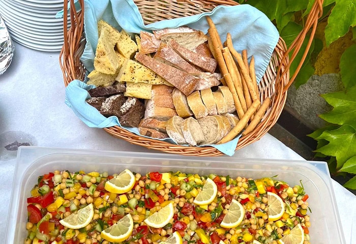 Korb mit Brot und Grissini, bunte Gemüsesalatplatte vorne, Zitronenscheiben als Garnitur.