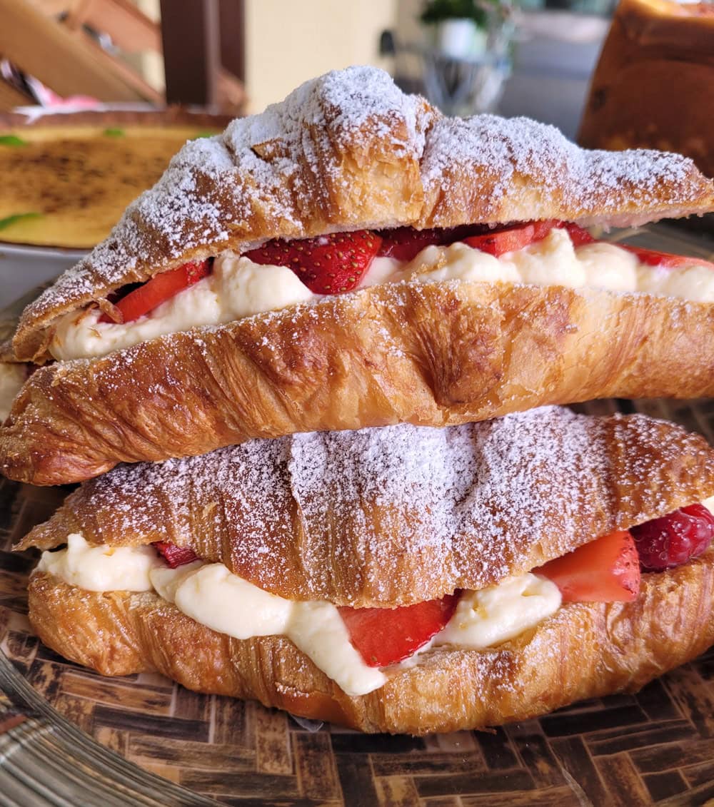 Zwei Croissants mit Erdbeeren und Sahne gefüllt, bestäubt mit Puderzucker, auf einem Teller.