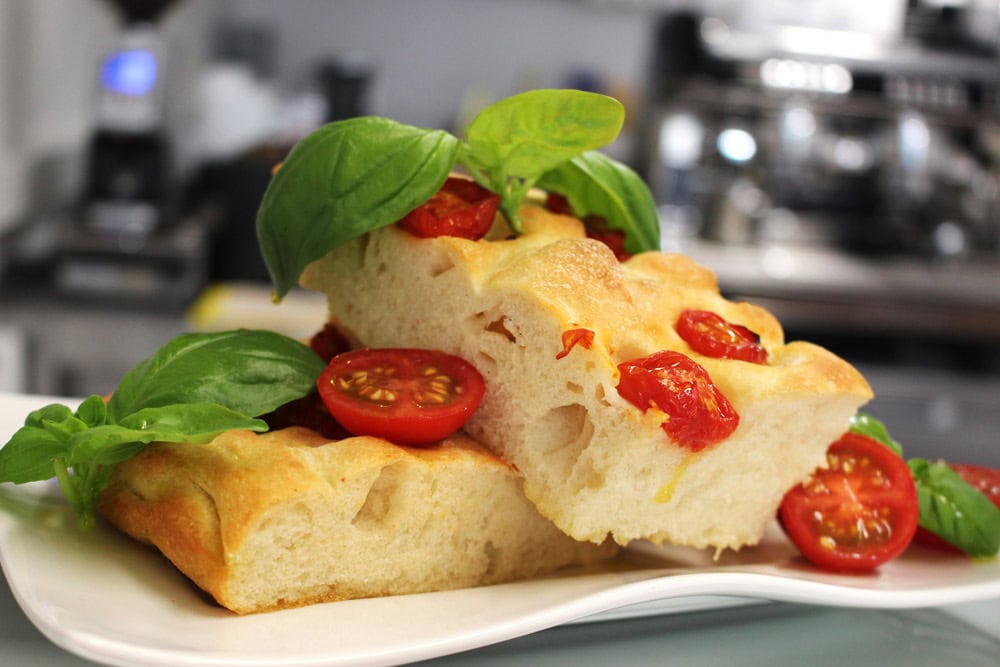 Focaccia mit Tomaten und Basilikum auf Teller, grob geschnitten, goldbraun und saftig.