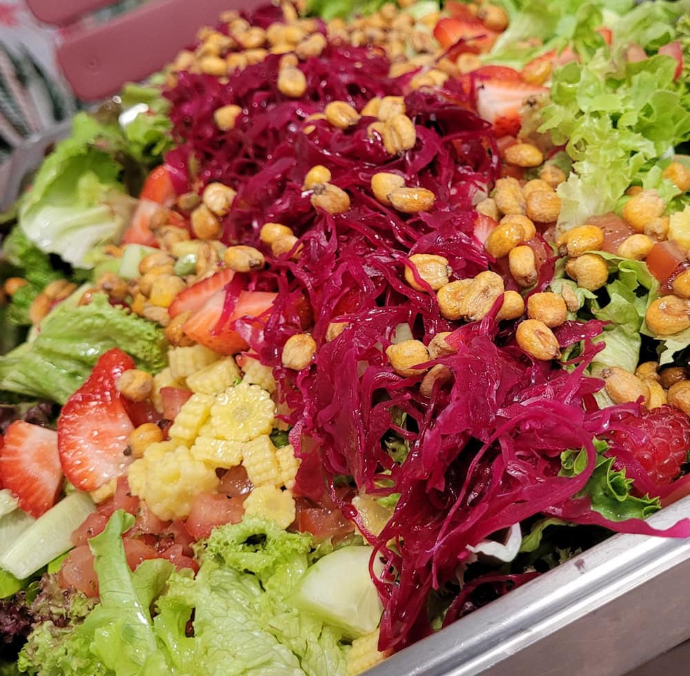 Ein bunter Salat mit Rotkohl, Erbsen, Erdbeeren und Salatblättern in lebhaften Farben.