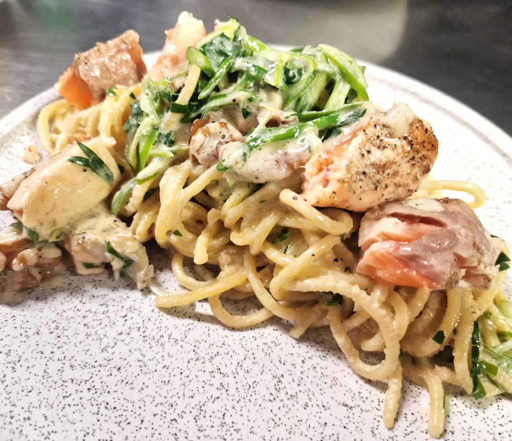 Spaghetti mit Lachs, Spinat und Sahnesoße auf einem weißen Teller.