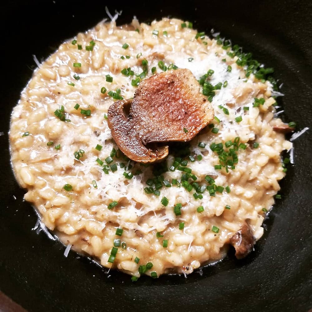 Cremiges Risotto mit Pilzen und Schnittlauch in einer schwarzen Schale.